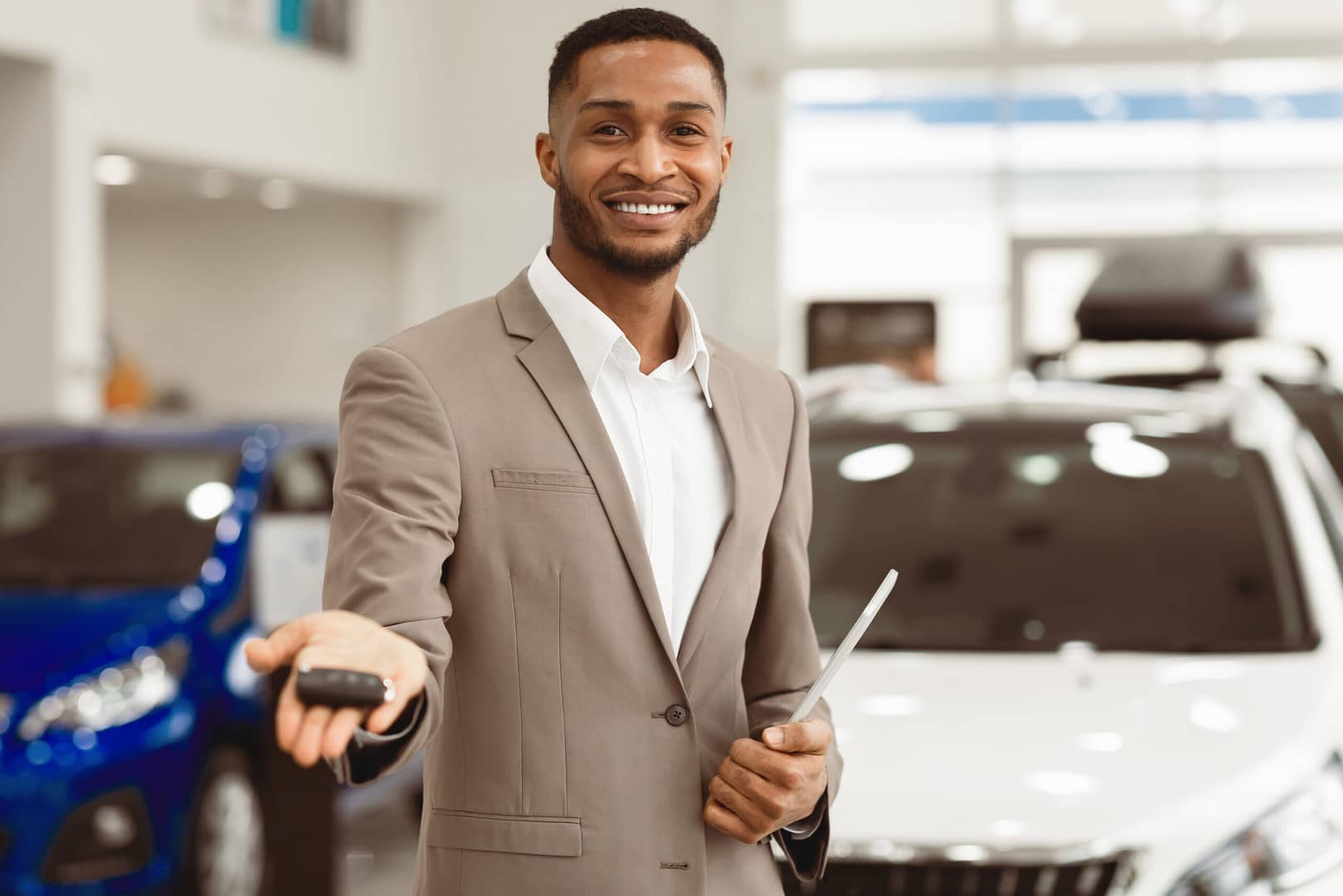 Car Dealer Offering Automobile Key To Camera Standing In Dealership